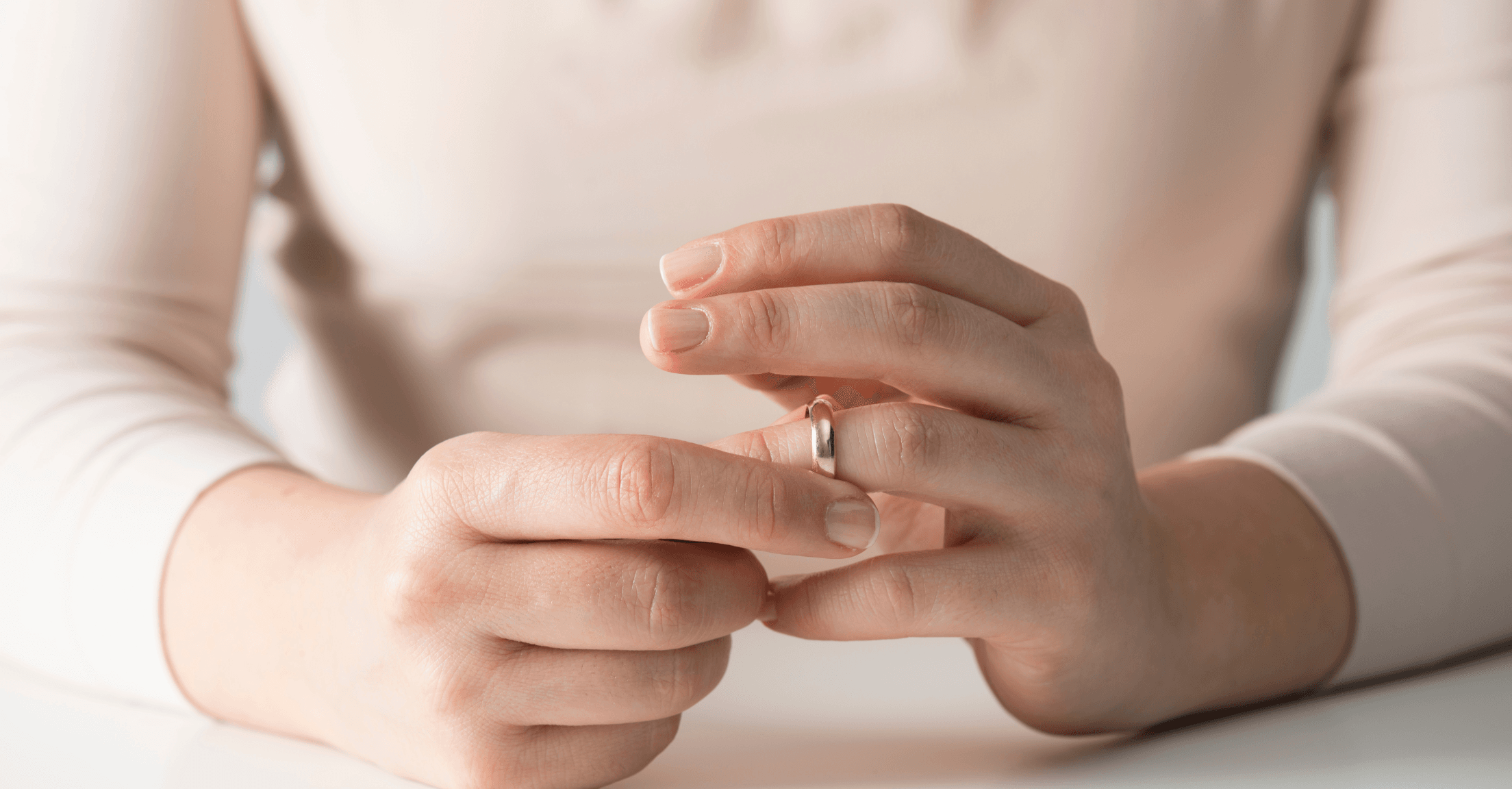 Close-up of a woman's hands, holding her wedding ring closer to the edge of her finger