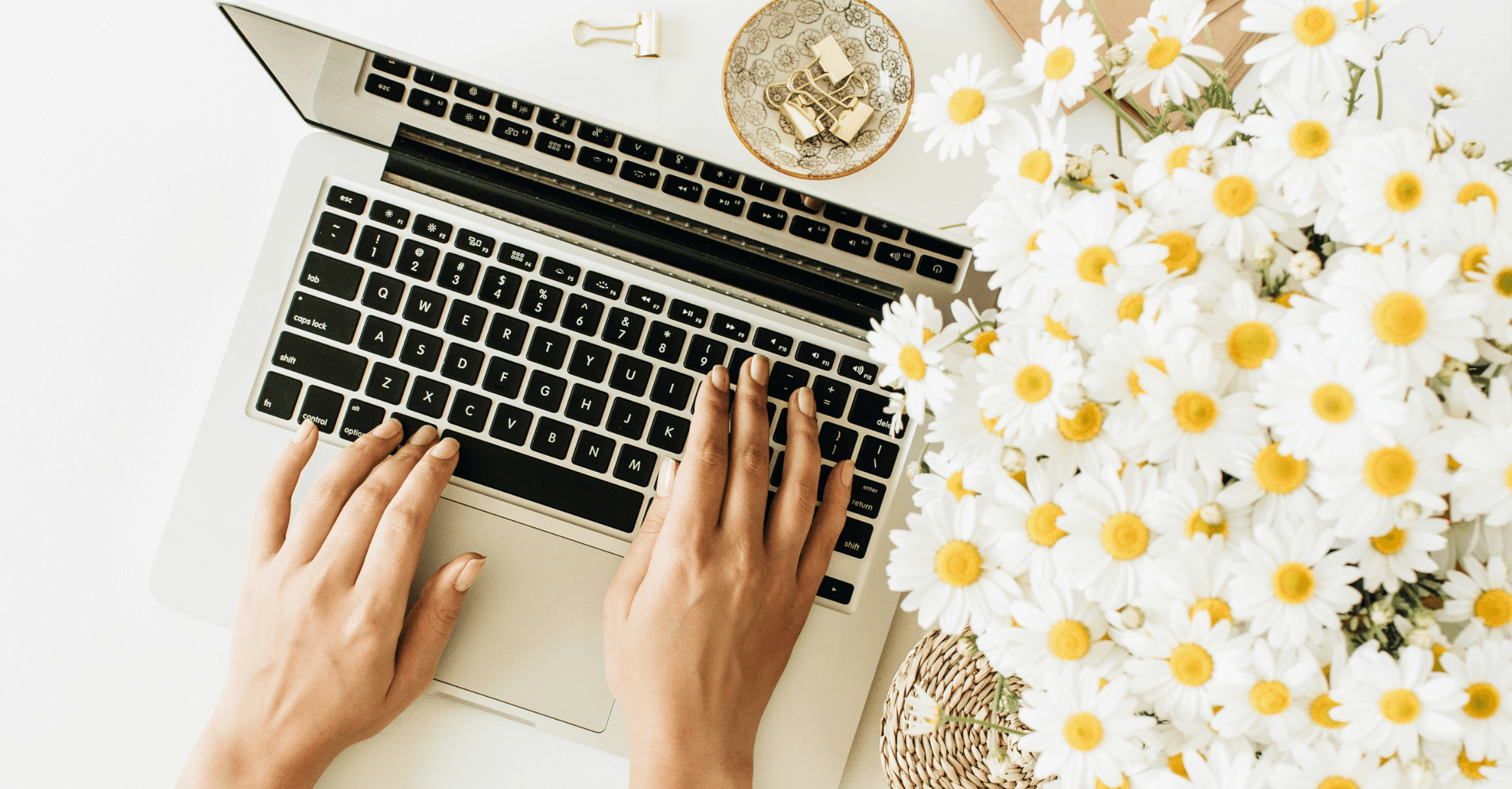 Women's hands typing on laptop, daisies next to her