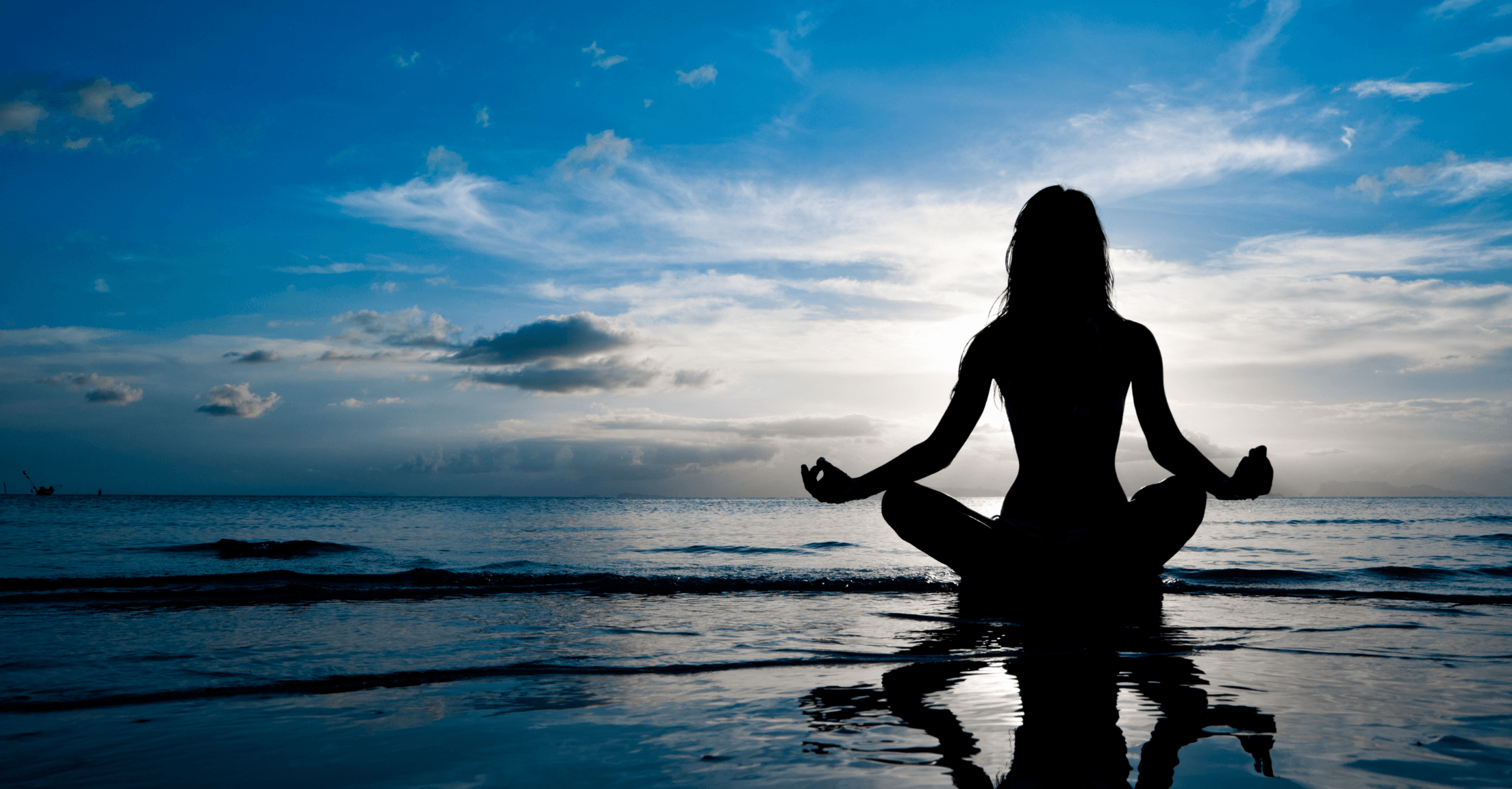 Woman sitting at the edge of the ocean meditating in a yoga lotus pose
