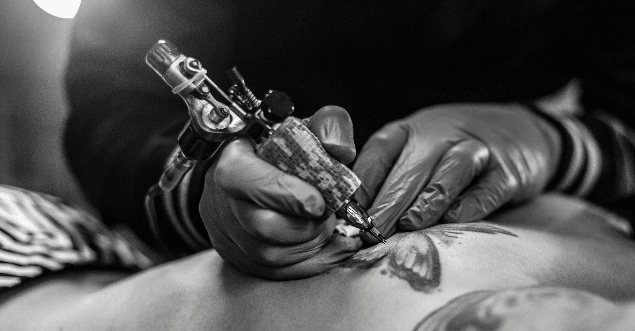 Black and white image of a tattoo artist inking a butterfly tattoo