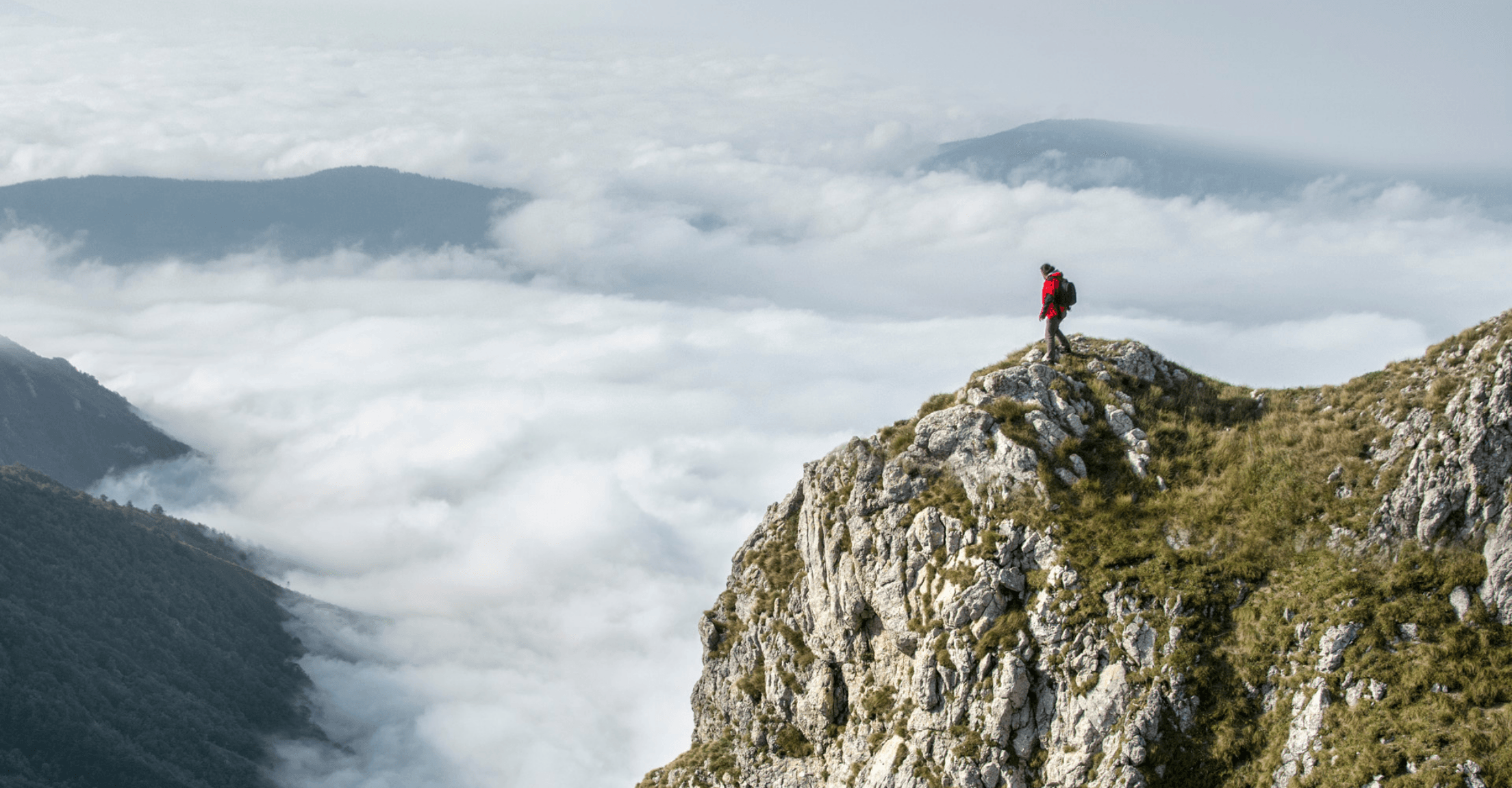 Hiker standing at mountain peak with clouds in background